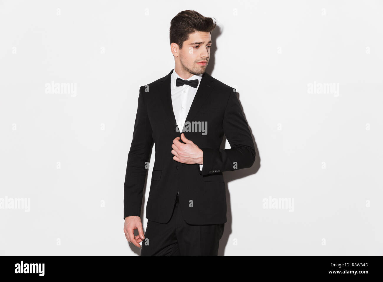 Portrait of a handsome young man wearing black suit with a bow standing ...