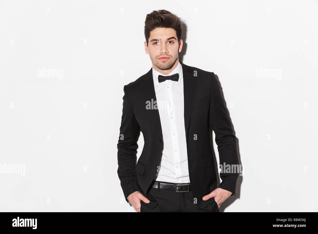 Portrait of a handsome young man wearing black suit with a bow standing ...