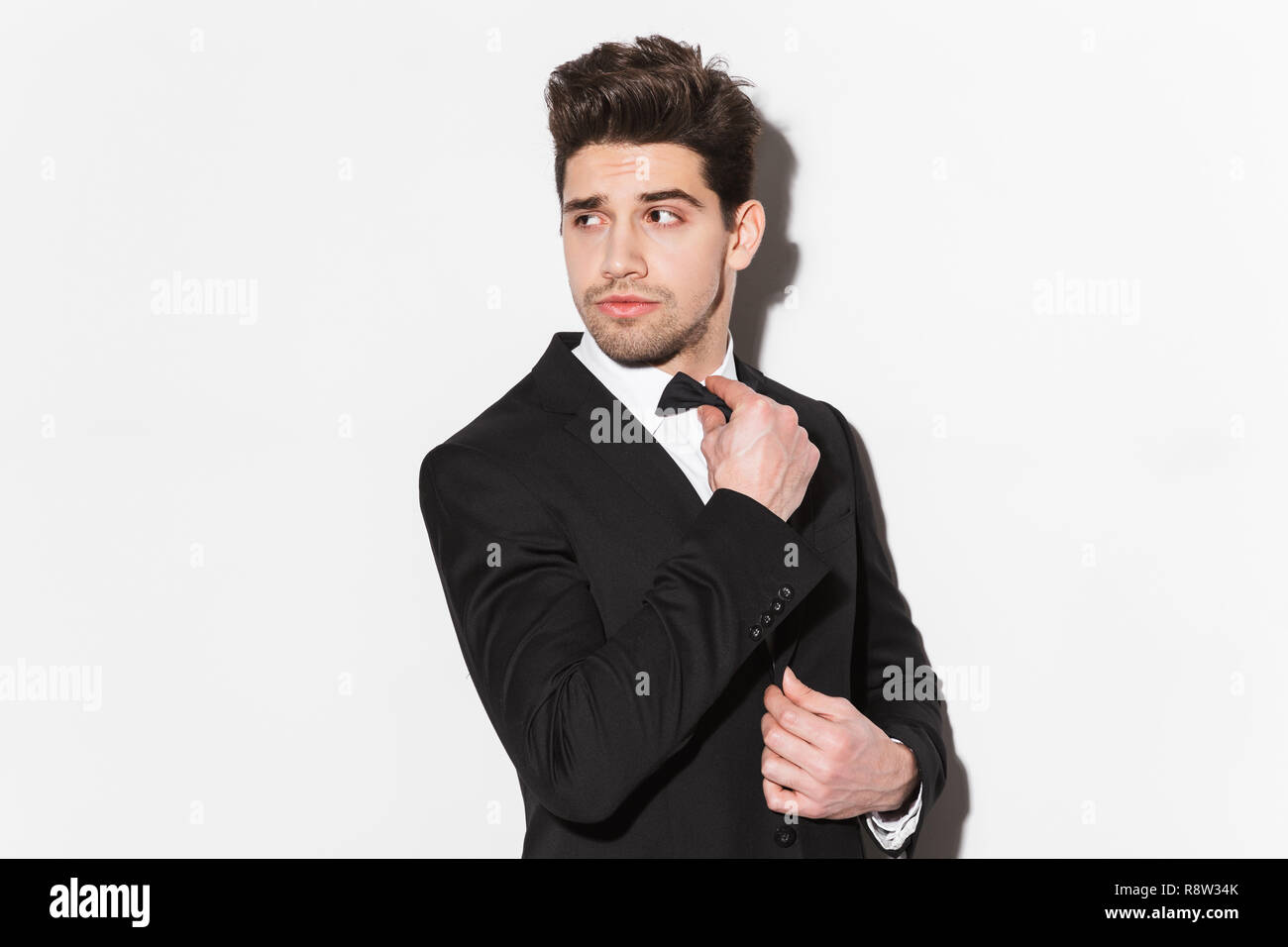 Portrait of a handsome young man wearing black suit with a bow standing ...
