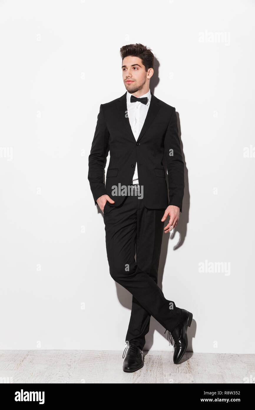 Full length portrait of a handsome young man wearing black suit with a ...