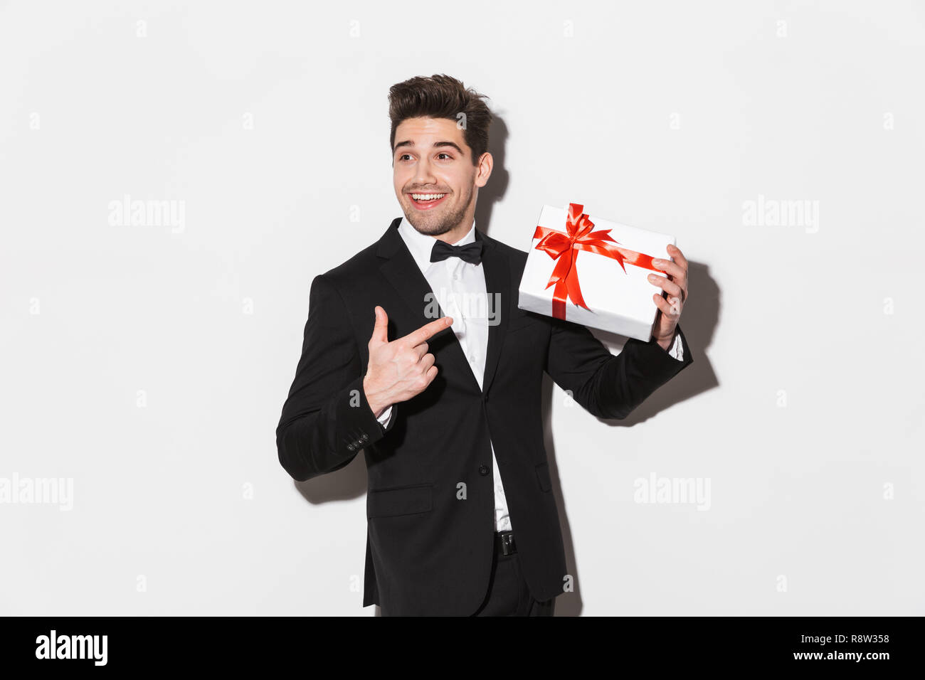 Portrait of a cheerful young man wearing black suit with a bow standing ...