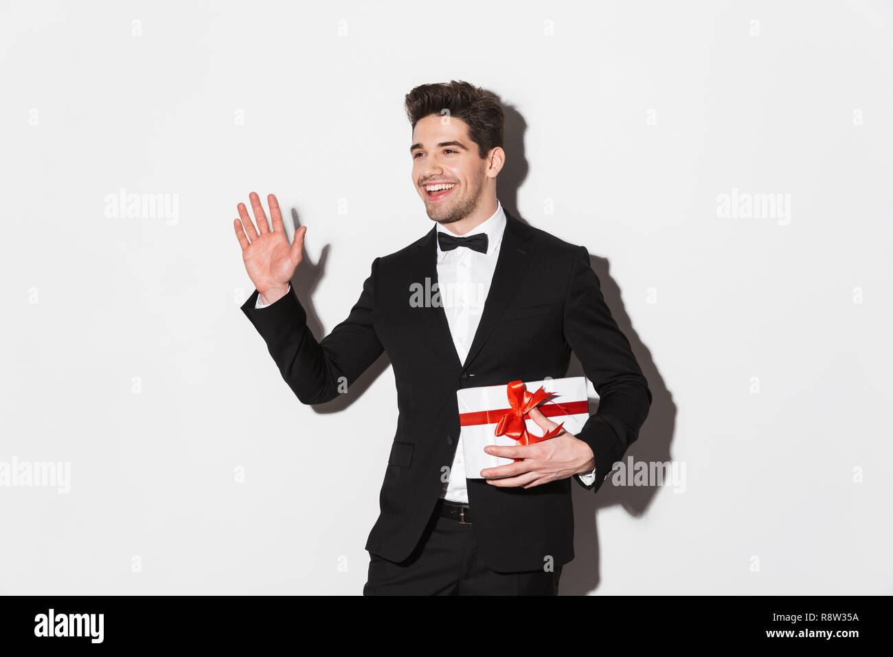 Portrait of a cheerful young man wearing black suit with a bow standing ...