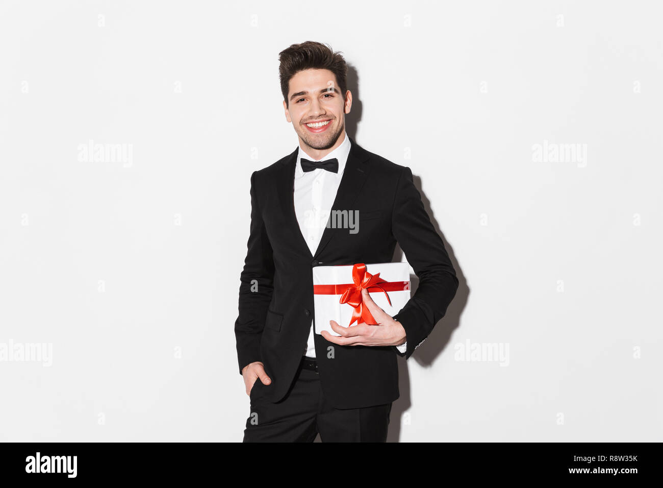 Portrait of a smiling young man wearing black suit with a bow standing ...