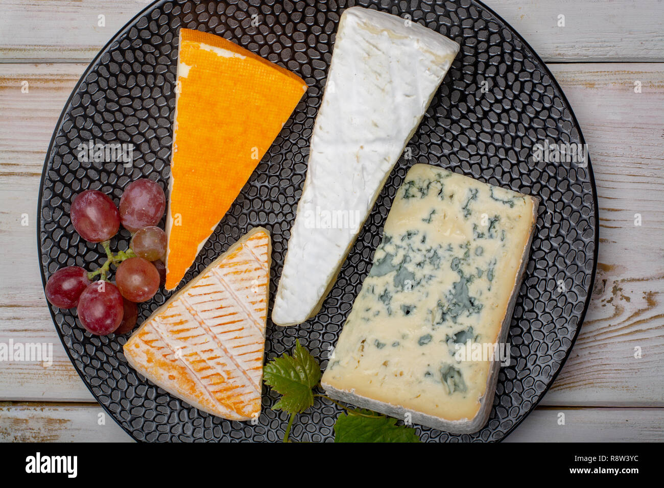 Tasting plate with four France cheeses, cream brie, marcaire, saint paulin and blue auvergne cheese, served with fresh ripe grapes close up Stock Photo