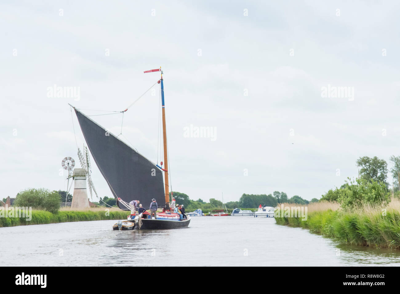 Wherry, traditional sailing boat on Norfolk Broads, River Thurne, in front of Thurne Dyke Drainage Mill. June. Stock Photo