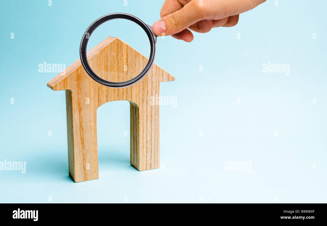 Magnifying glass is looking at the Wooden house on a blue background. Lending to the public. The concept of affordable housing and mortgages to buy a  Stock Photo