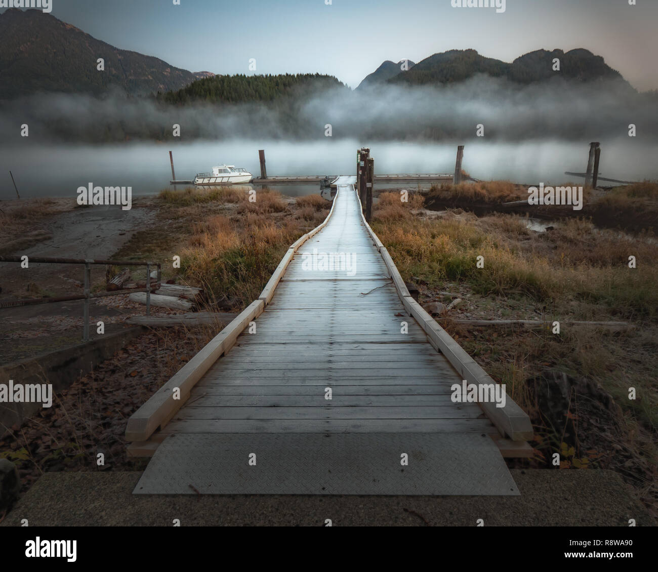 Dock leading to a foggy river with mountains along shore in Pitt Meadows. Stock Photo