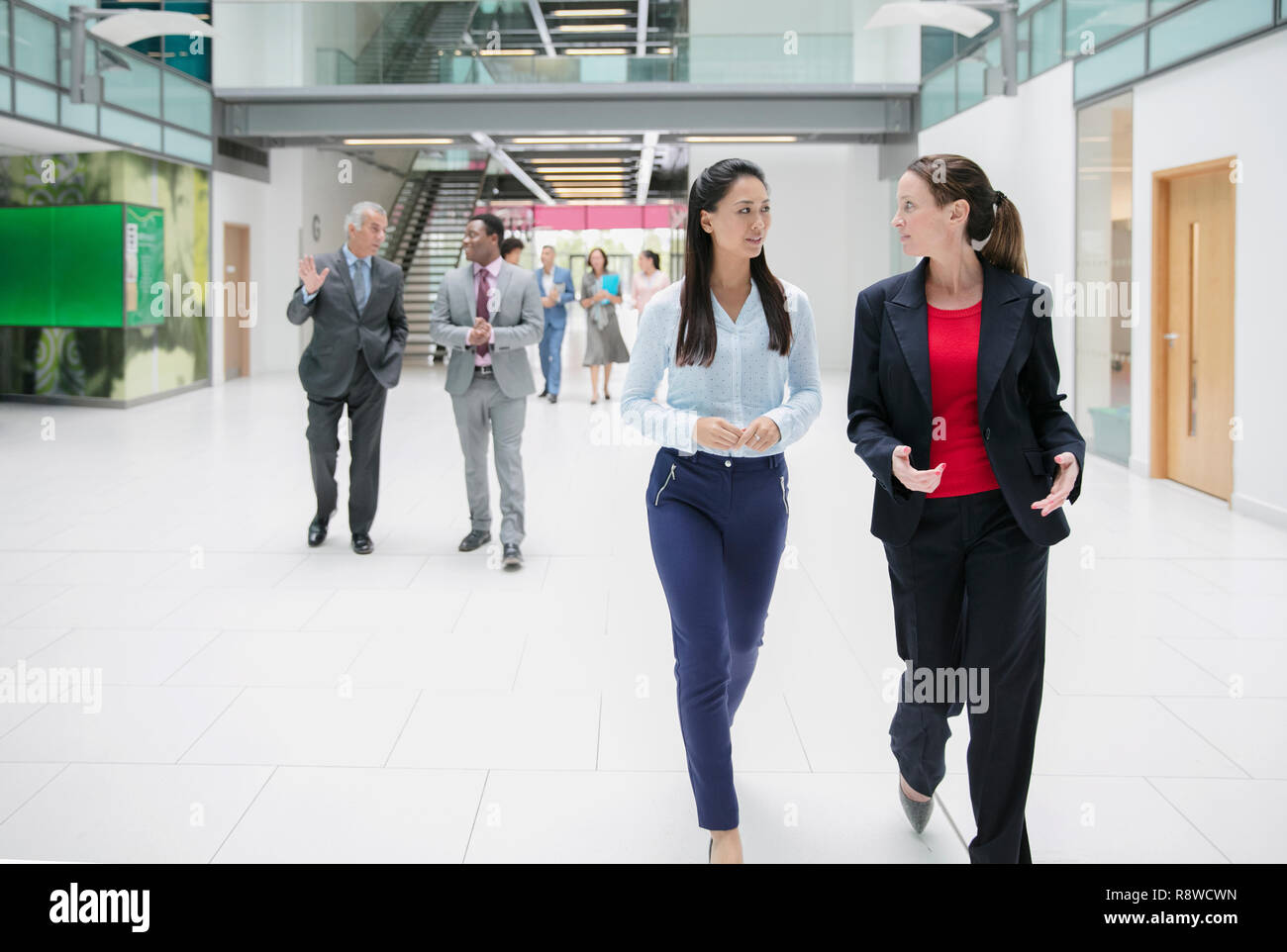 Businesswomen walking and talking in office lobby Stock Photo
