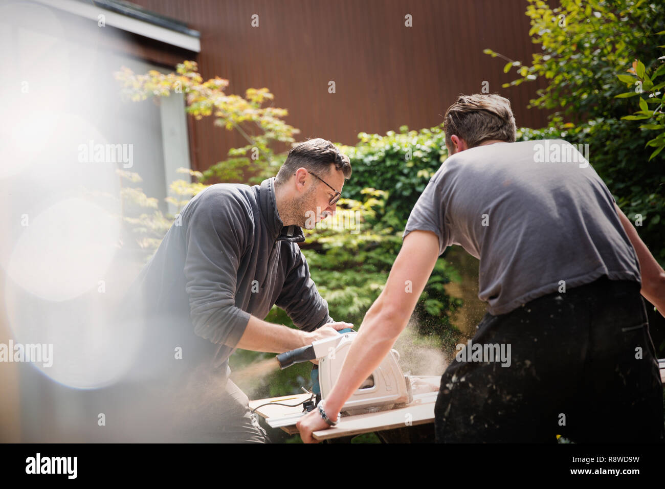 Construction workers using table saw to cut wood in driveway Stock Photo
