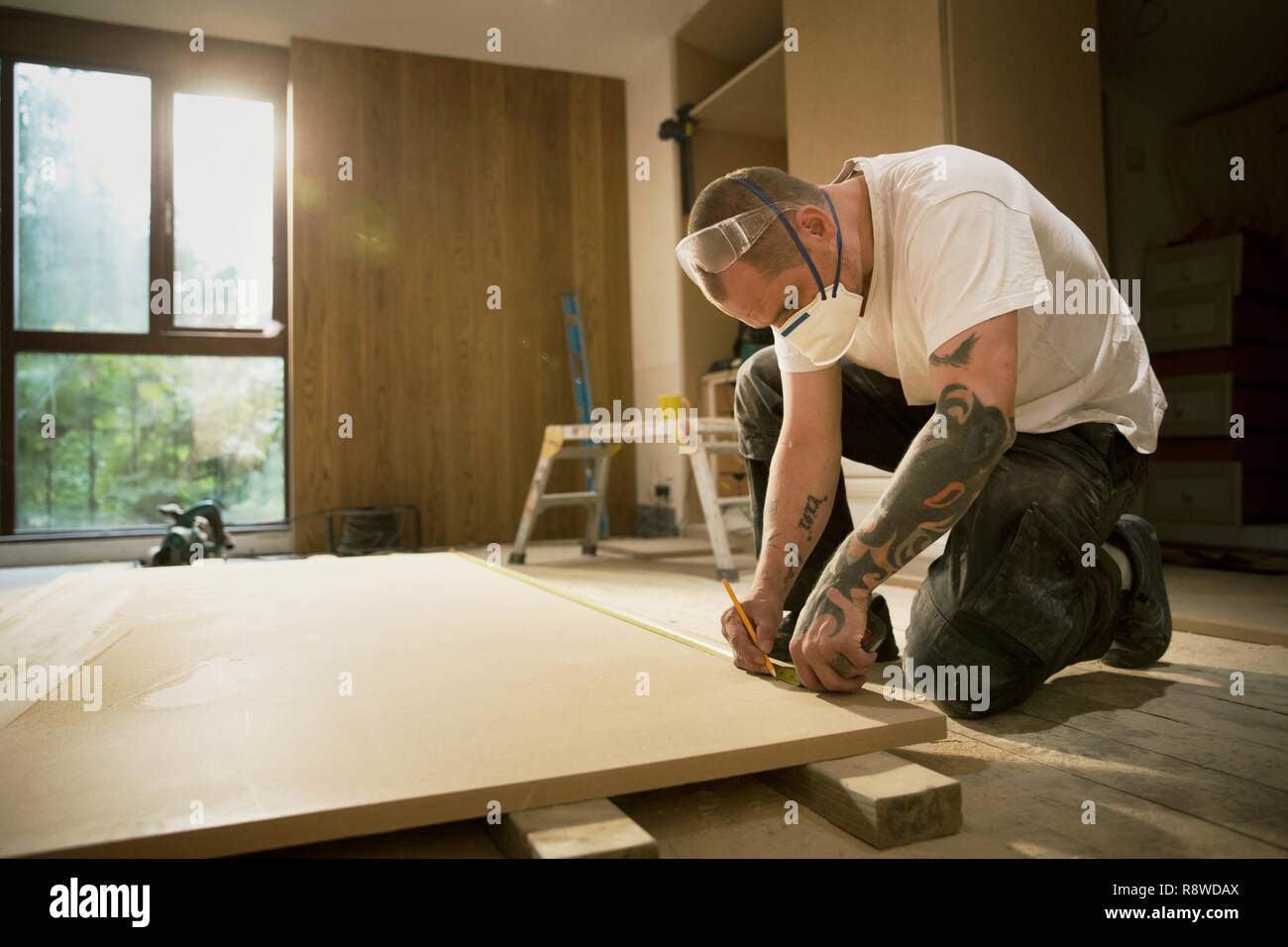 Construction worker with tattoos measuring and marking wood board in house Stock Photo