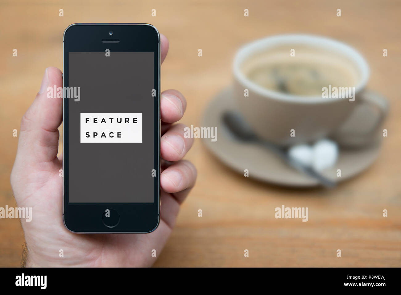 A man looks at his iPhone which displays the Feature Space logo (Editorial use only). Stock Photo