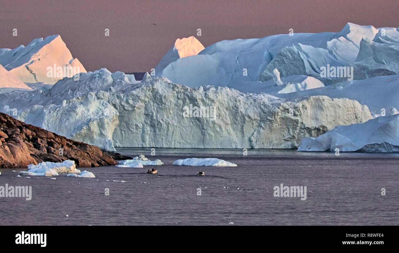 Ilulissat Eisberge am Abend Lichtkunst vom Feinsten. Kleine Ausflugsboote bringen die Touristen direkt an die weißen Riesen Stock Photo