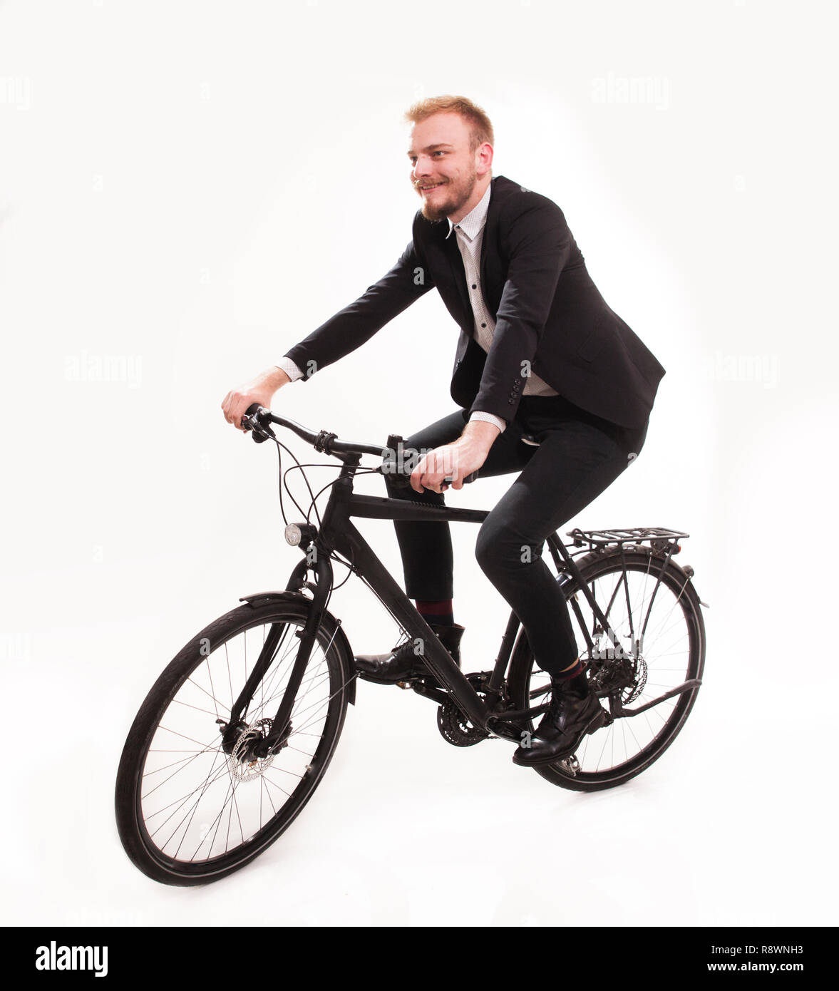 one young smiling man, 20-29 years, dressed in suit, formal wear. sitting on a bike, cycling in studio on isolated white background. Stock Photo