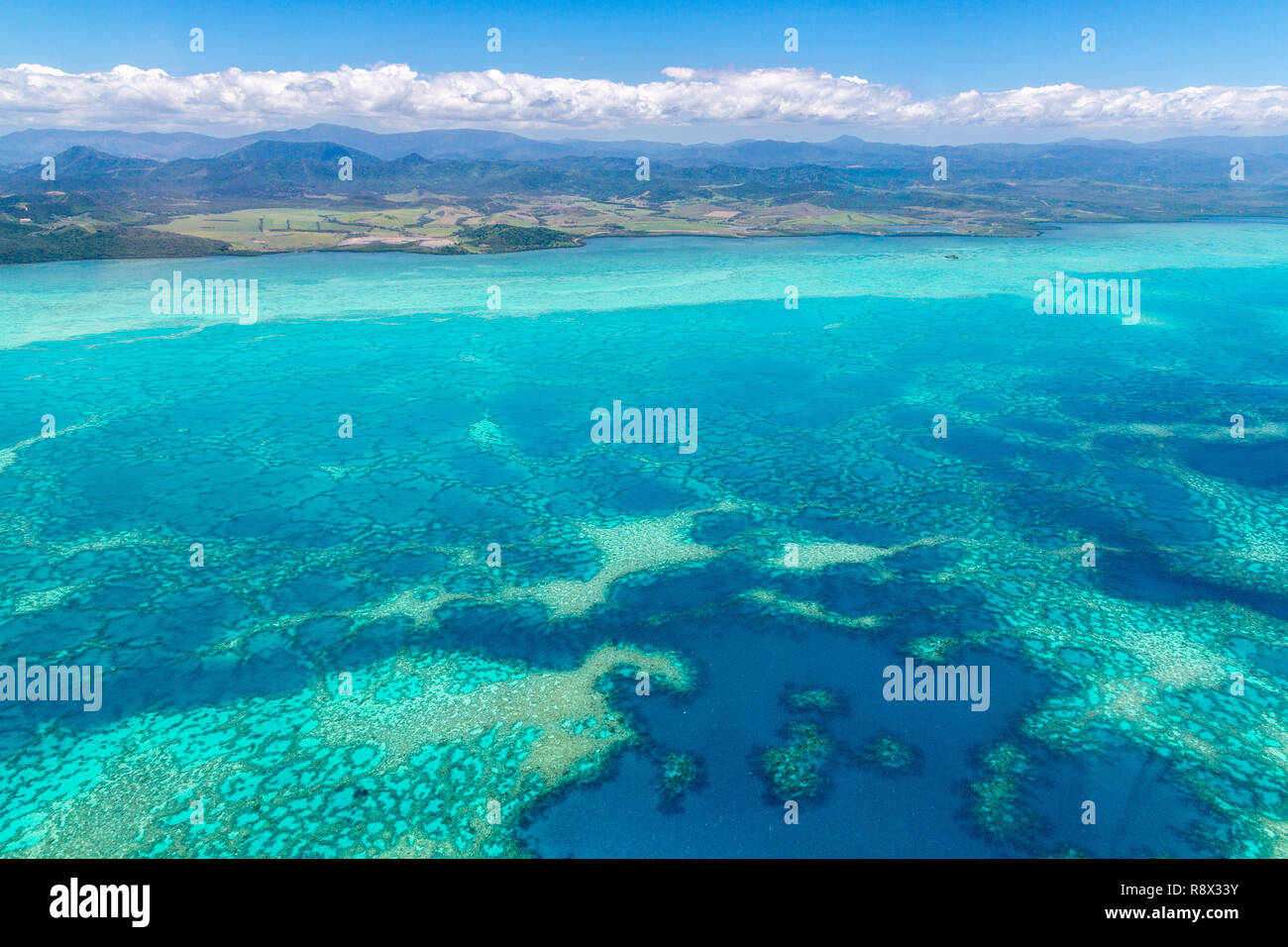 Aerial view of idyllic azure turquoise blue lagoon of West Coast barrier reef, with mountains far in the background, Coral sea, New Caledonia island,  Stock Photo