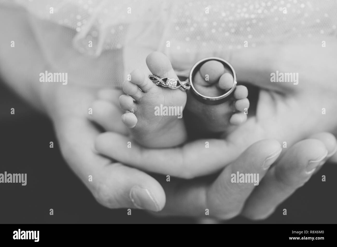 Wedding Rings on Newborn Baby Feet with Parents Hands Holding Stock Photo