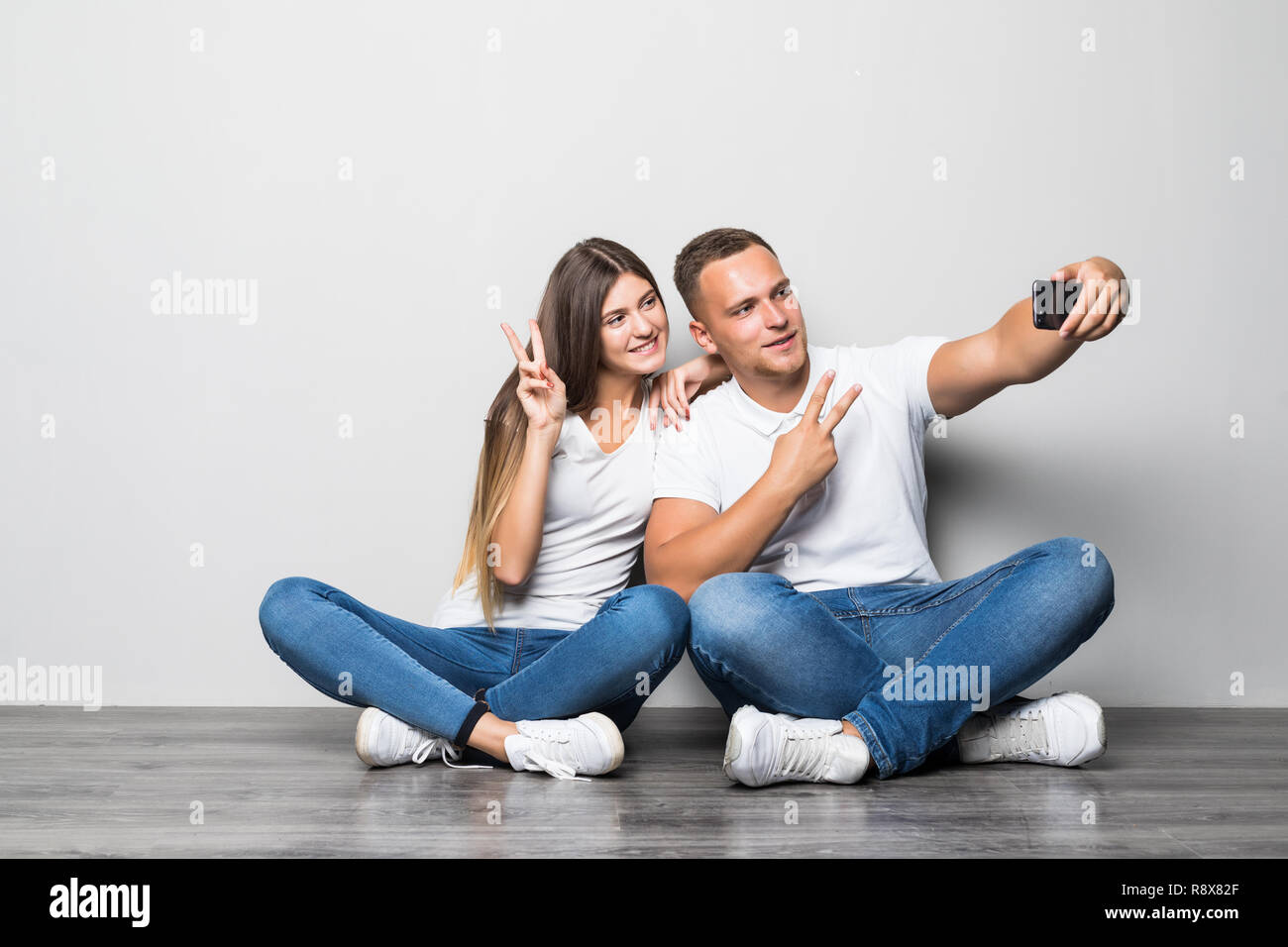 Portrait of a happy young couple sitting together over beige background, taking selfies Stock Photo