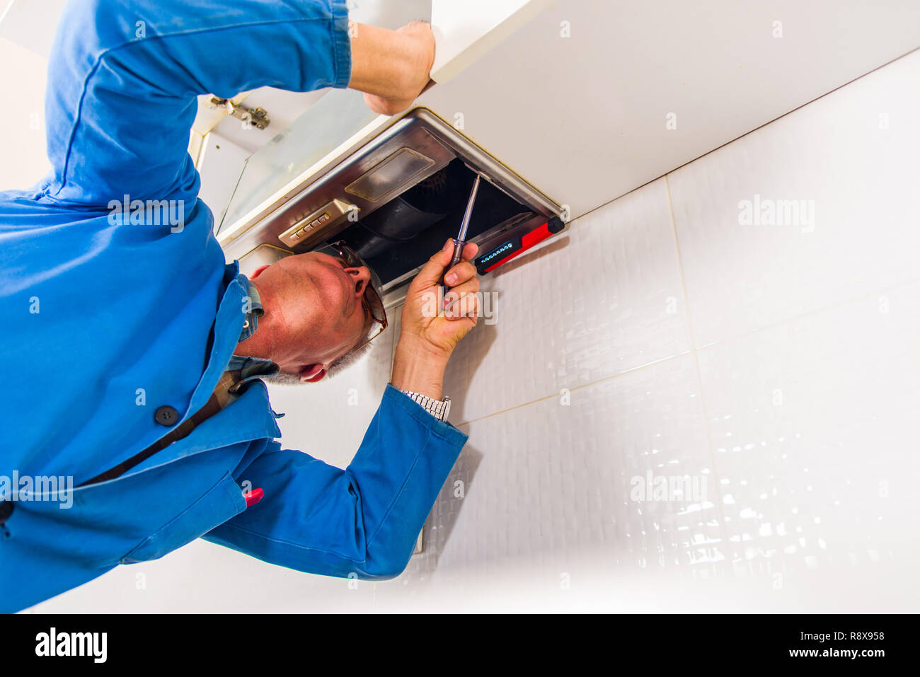 Mature workman fixing vent with worktool in kitchen Stock Photo