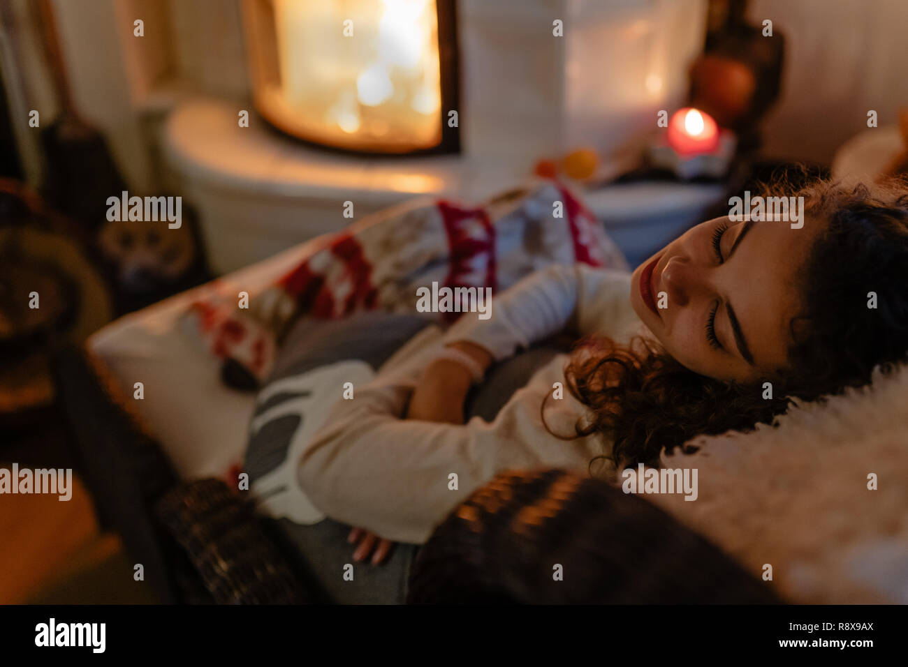 Beautiful young woman with curly hair is taking a nap with fireplace in the back Stock Photo