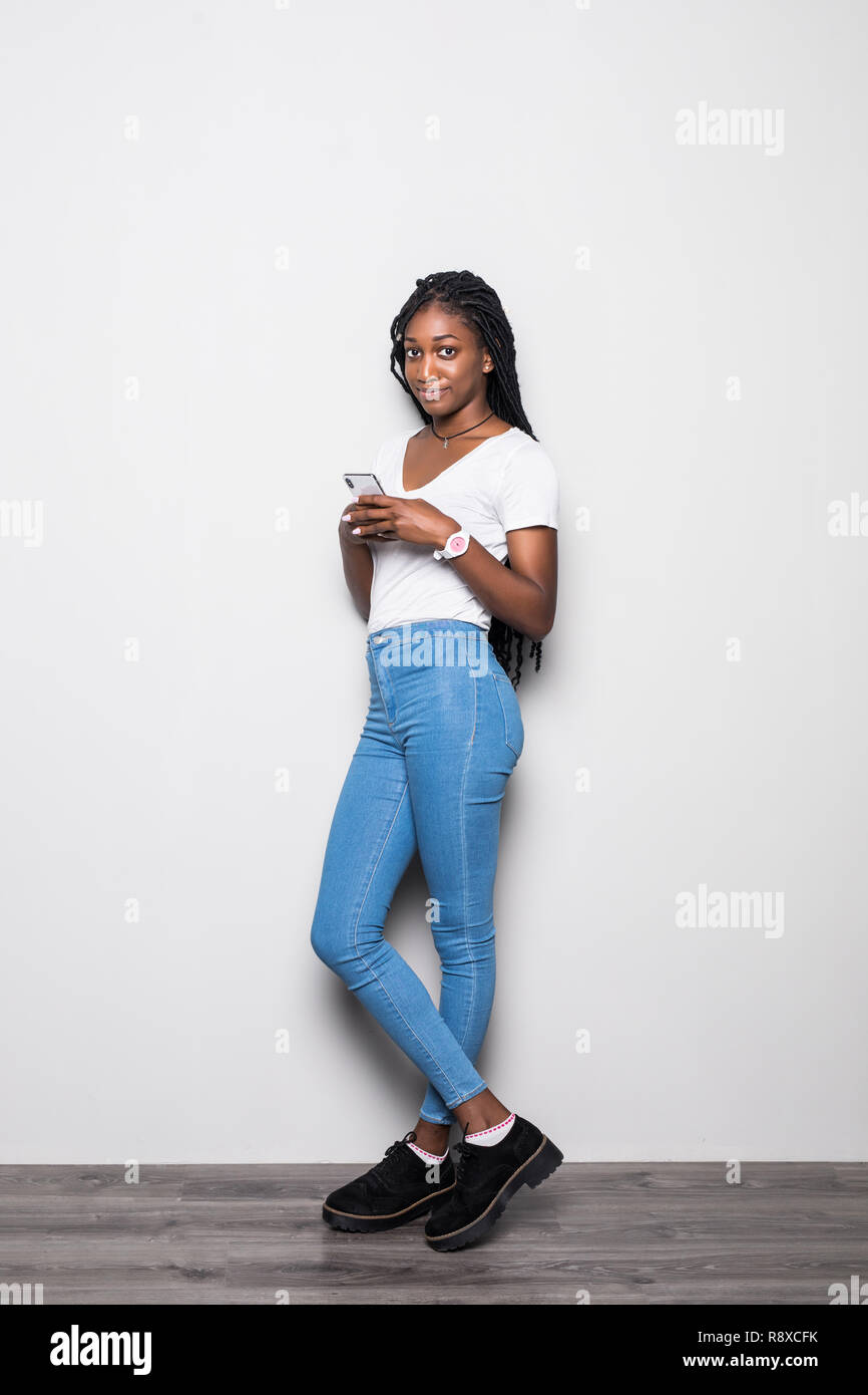 Full length portrait of woman with afro hairstyle wearing t-shirt and jeans  using smartphone isolated over white background Stock Photo - Alamy