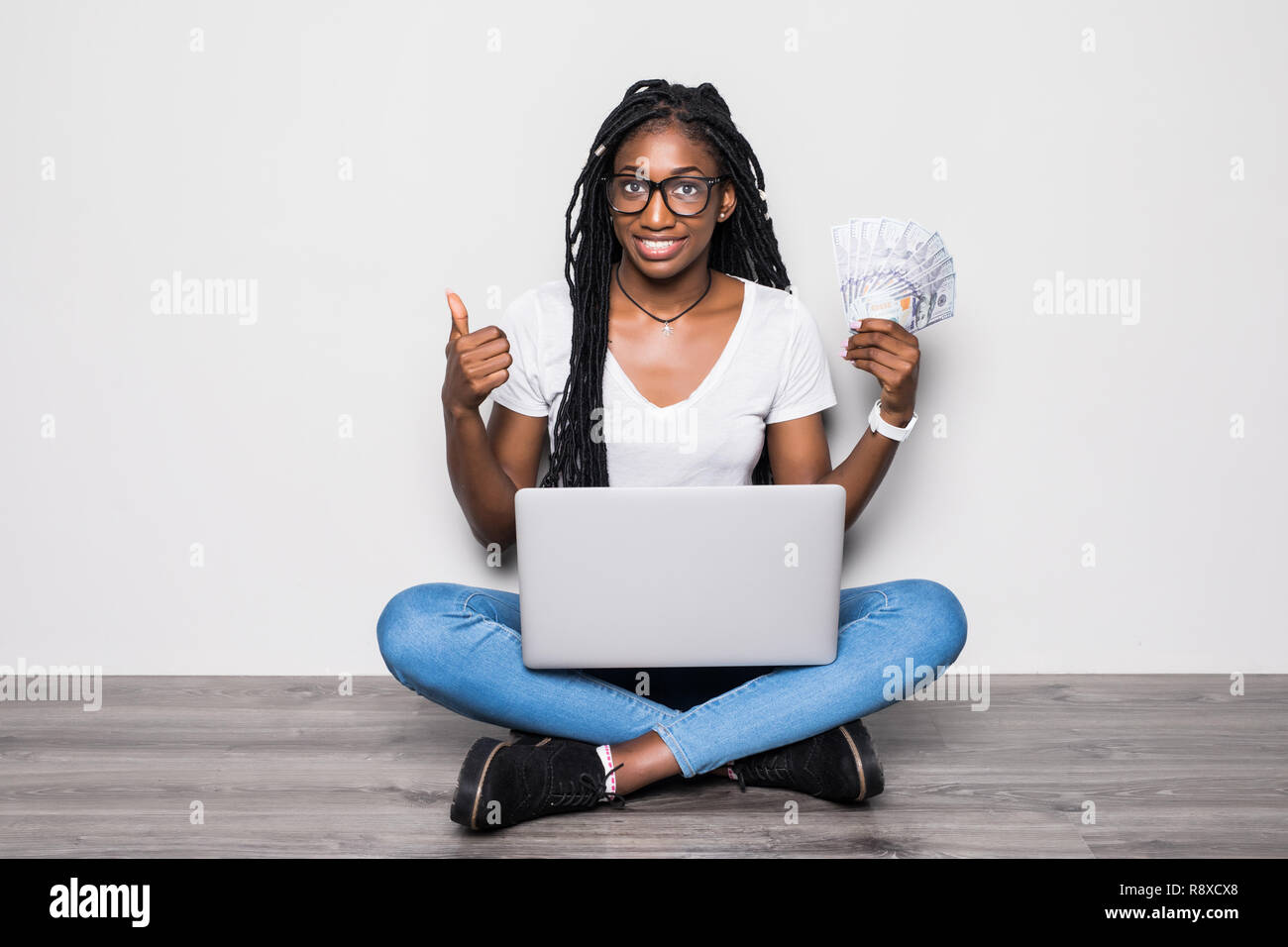 Full length portrait of young afro american woman sitting on floor hold money pc ion gray background Stock Photo