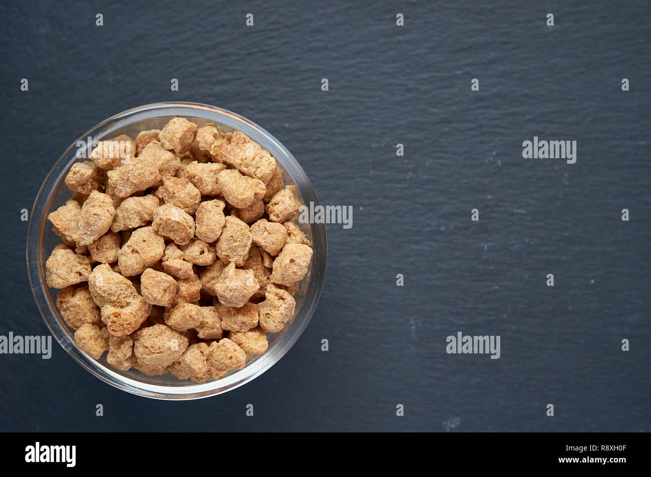 Healthy, nutritious soybean meat, chunks in a white bowl. Top view of raw soya chunks in bowl on dark background. Stock Photo