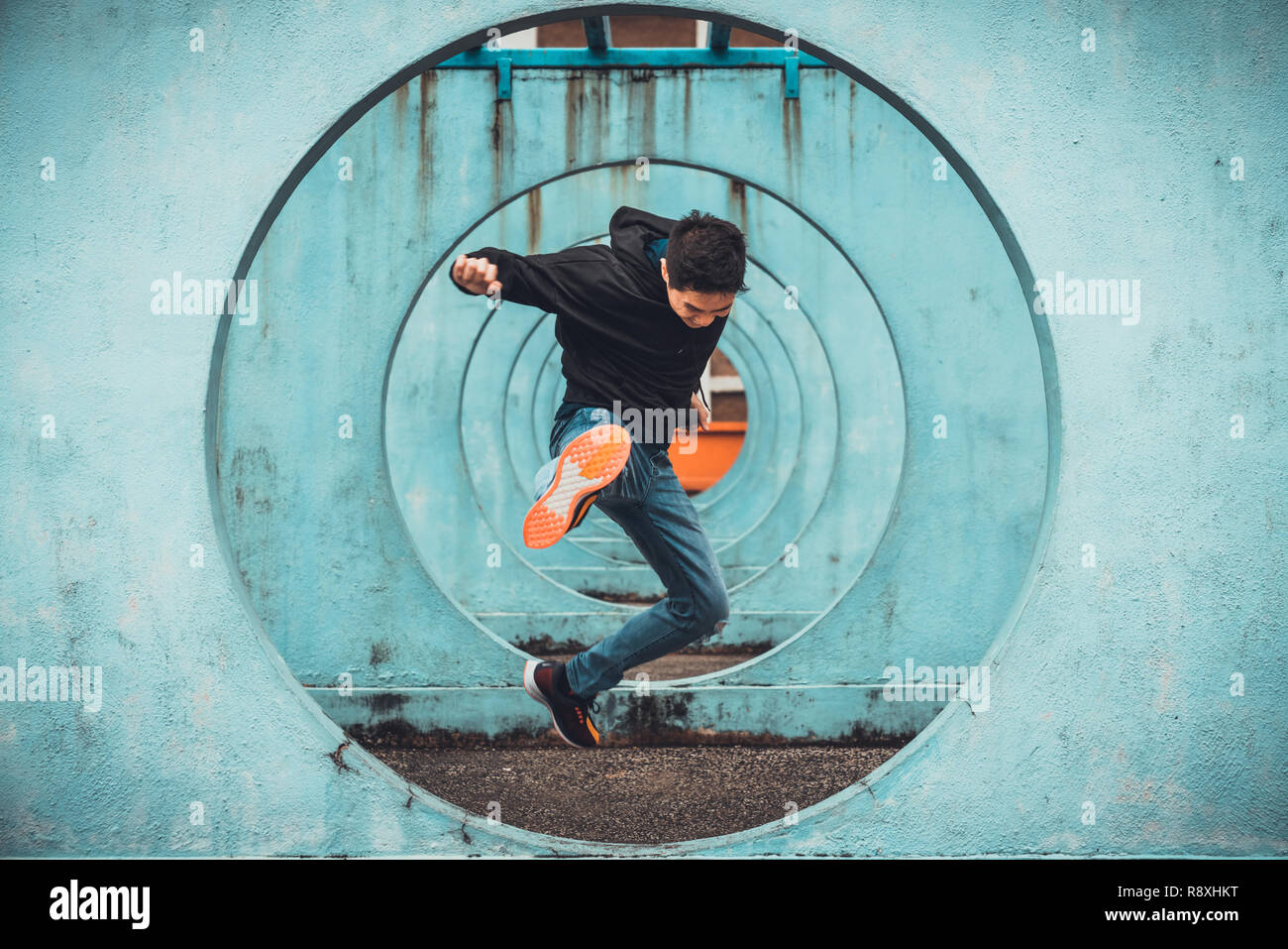 Young Asian active man jumping and kicking action, circle looping wall background. Extreme sport activity, healthy lifestyle, or parkour concept Stock Photo