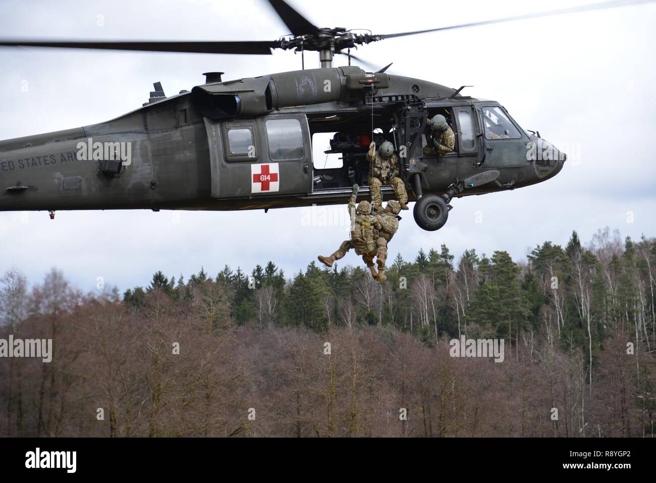A UH-60 Blackhawk, operated by U.S. Soldiers, assigned to 12th Combat Aviation Brigade, hoists U.S. Soldiers, assigned to the 1st Squadron, 2nd Cavalry Regiment, as they conduct different types of Medical Evacuations, at the 7th Army Training Command’s Grafenwoehr Training Area, Germany, Feb. 28, 2017. The Soldiers conducted MEDEVAC training to develop the ability to team up with flight medics to safely transport patients by a helicopter. Stock Photo