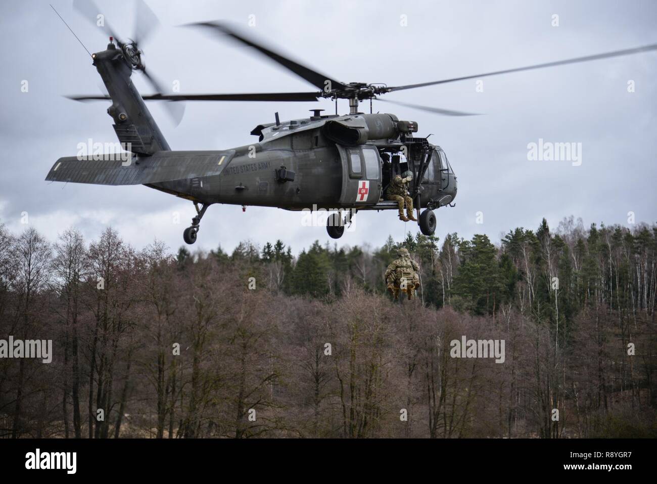 A UH-60 Blackhawk, operated by U.S. Soldiers, assigned to 12th Combat Aviation Brigade, hoists U.S. Soldiers, assigned to the 1st Squadron, 2nd Cavalry Regiment, as they conduct different types of Medical Evacuations, at the 7th Army Training Command’s Grafenwoehr Training Area, Germany, Feb. 28, 2017. The Soldiers conducted MEDEVAC training to develop the ability to team up with flight medics to safely transport patients by a helicopter. Stock Photo
