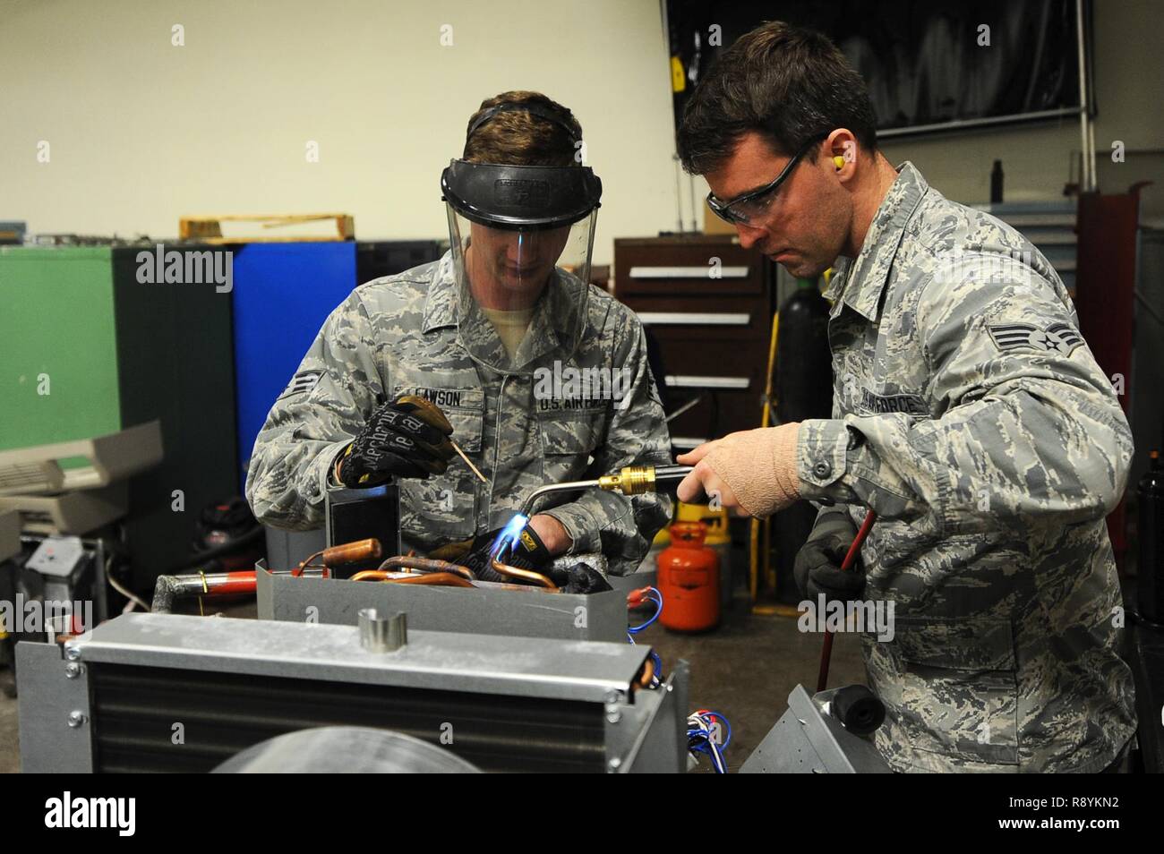Senior Airman Tate Lawson and Senior Airman Michael Robinson, 5th Civil  Engineer heating, ventilation, air conditioning and refrigeration  technicians, solder valves onto a heating and cooling unit at Minot Air  Force Base,