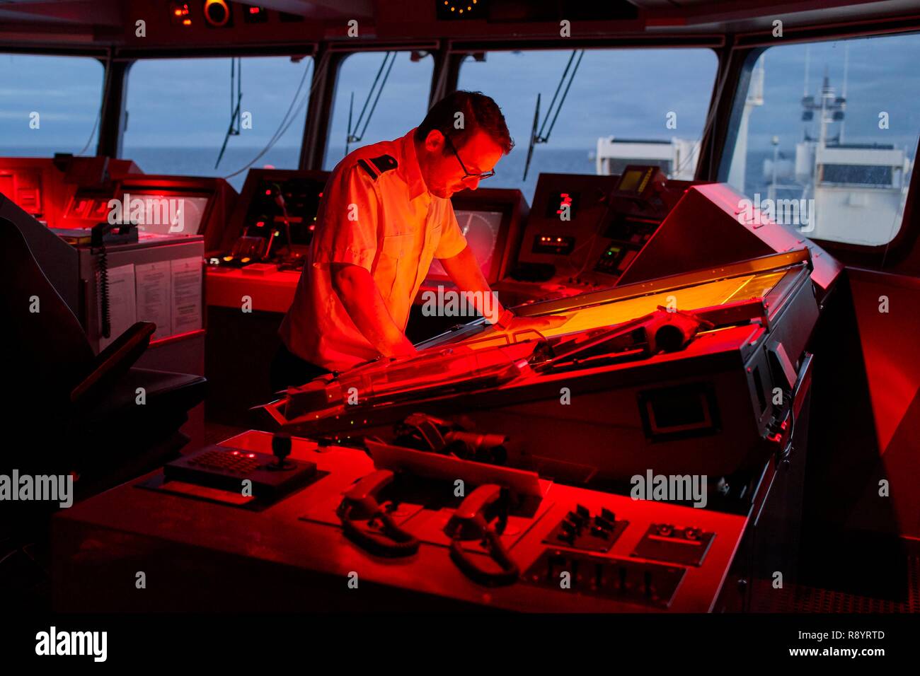 France, French Southern and Antarctic Territories (TAAF), Marion Dufresne II (supply ship of the TAAF), At the bridge, Alexandre LE BOUCHER (Lieutenant Commissioner) is at the chart table at dusk, The red lights allow to do not be dazzled so as not to degrade night vision Stock Photo