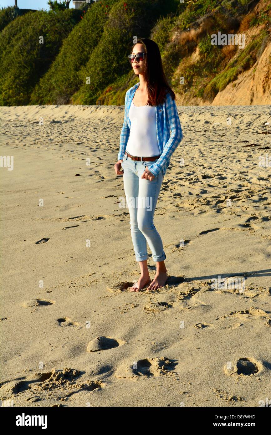young-barefoot-woman-wearing-sunglasses-and-jeans-is-standing-on-the-beach-in-laguna-beach-california-R8YWHD.jpg