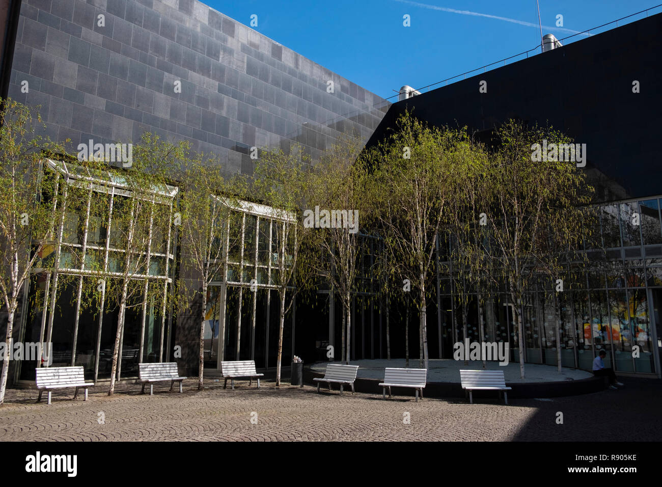 young birch trees and white park benches in front of the black outer wall in the courtyard of the K20 Kunstsammlung NRW, Dusseldorf, Germany Stock Photo
