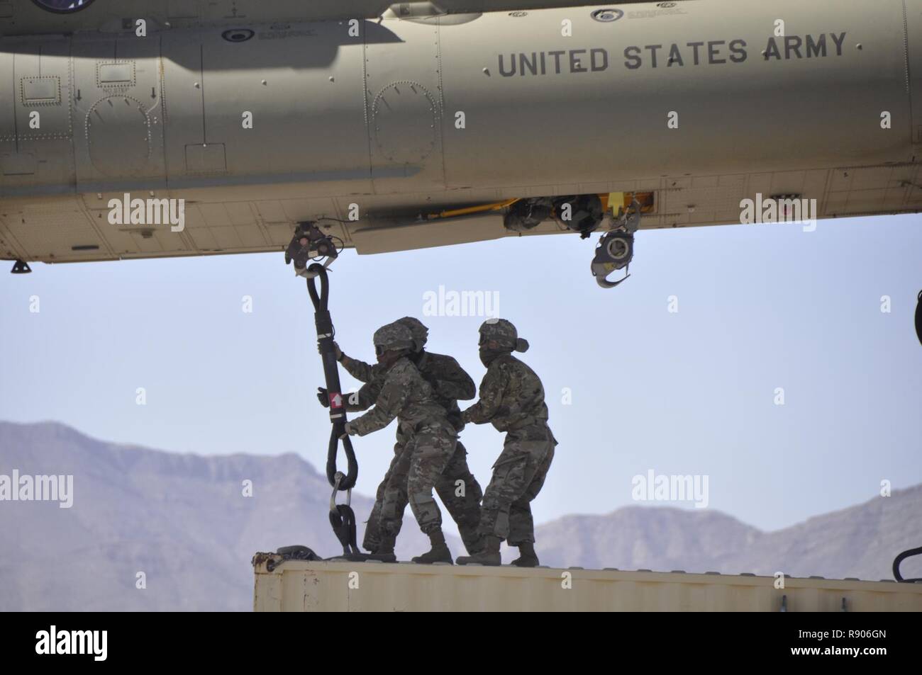 Spc. Sharnell Garrett, left front, assigned to Headquarters and Headquarters Company, Special Troops Battalion, 1st Armored Division Sustainment Brigade, attaches a Conex box to a CH-47 Chinook with two fellow Soldiers during sling load training at Biggs Army Airfield, Fort Bliss, Texas, March 10, 2017. Stock Photo