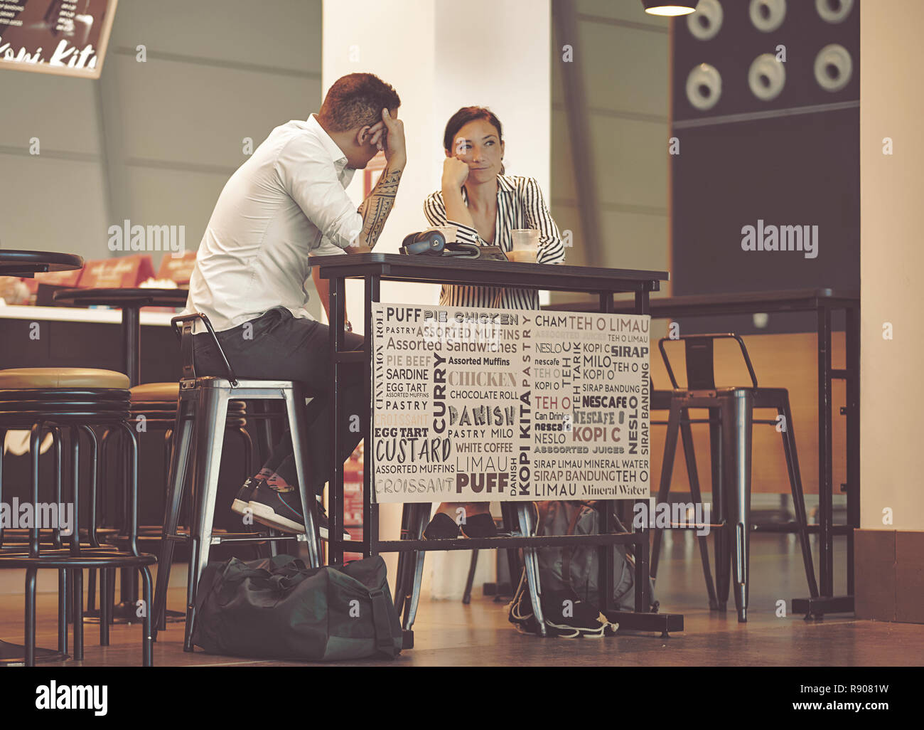 Doha, Qatar - December 9, 2018: beautiful young couple sitting in an airport cafe. Interracial couple talking in coffee shop. Couple sitting at table  Stock Photo