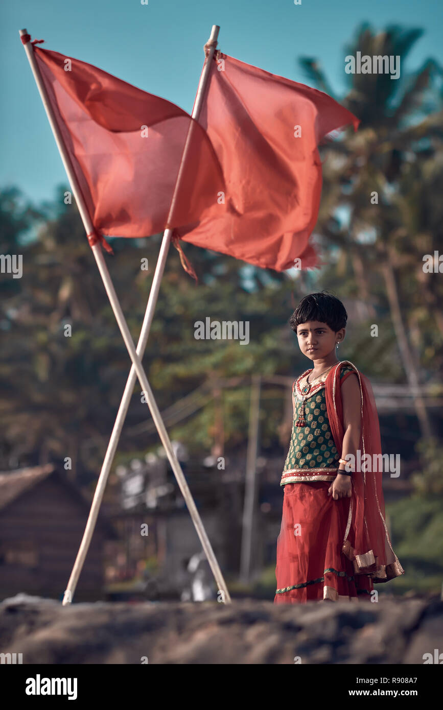 Varkala, Kerala / India – November 30, 2017: Portrait of Indian rural girl. Cute Indian girl dressed in sari, standing under red flags. Hipster color  Stock Photo