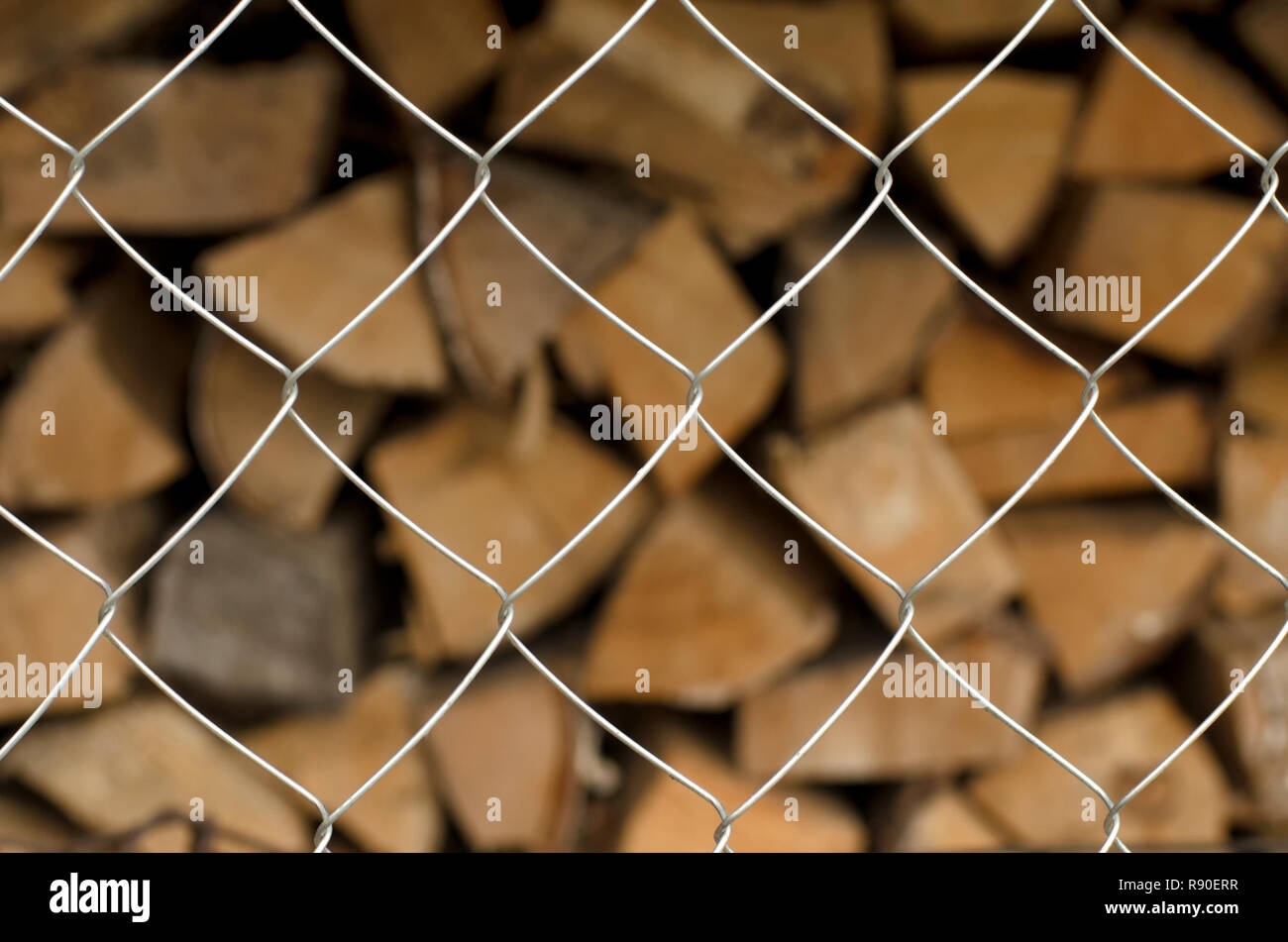Monotonous metal mesh cells in the foreground and a diversity of firewood on a blurred background Stock Photo