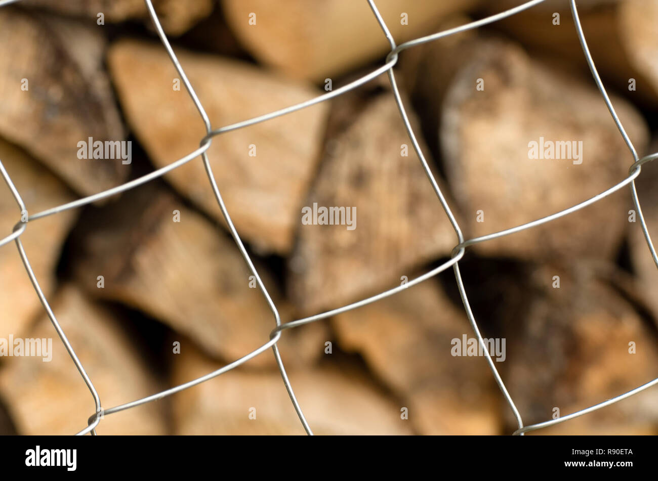 Monotonous metal mesh cells in the foreground and a diversity of firewood on a blurred background closeup Stock Photo