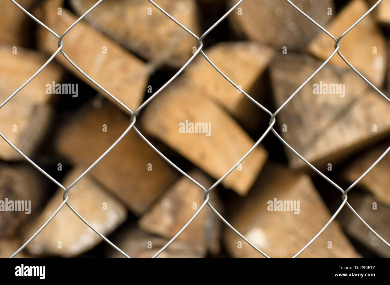 Monotonous metal mesh cells in the foreground and a diversity of firewood on a blurred background Stock Photo