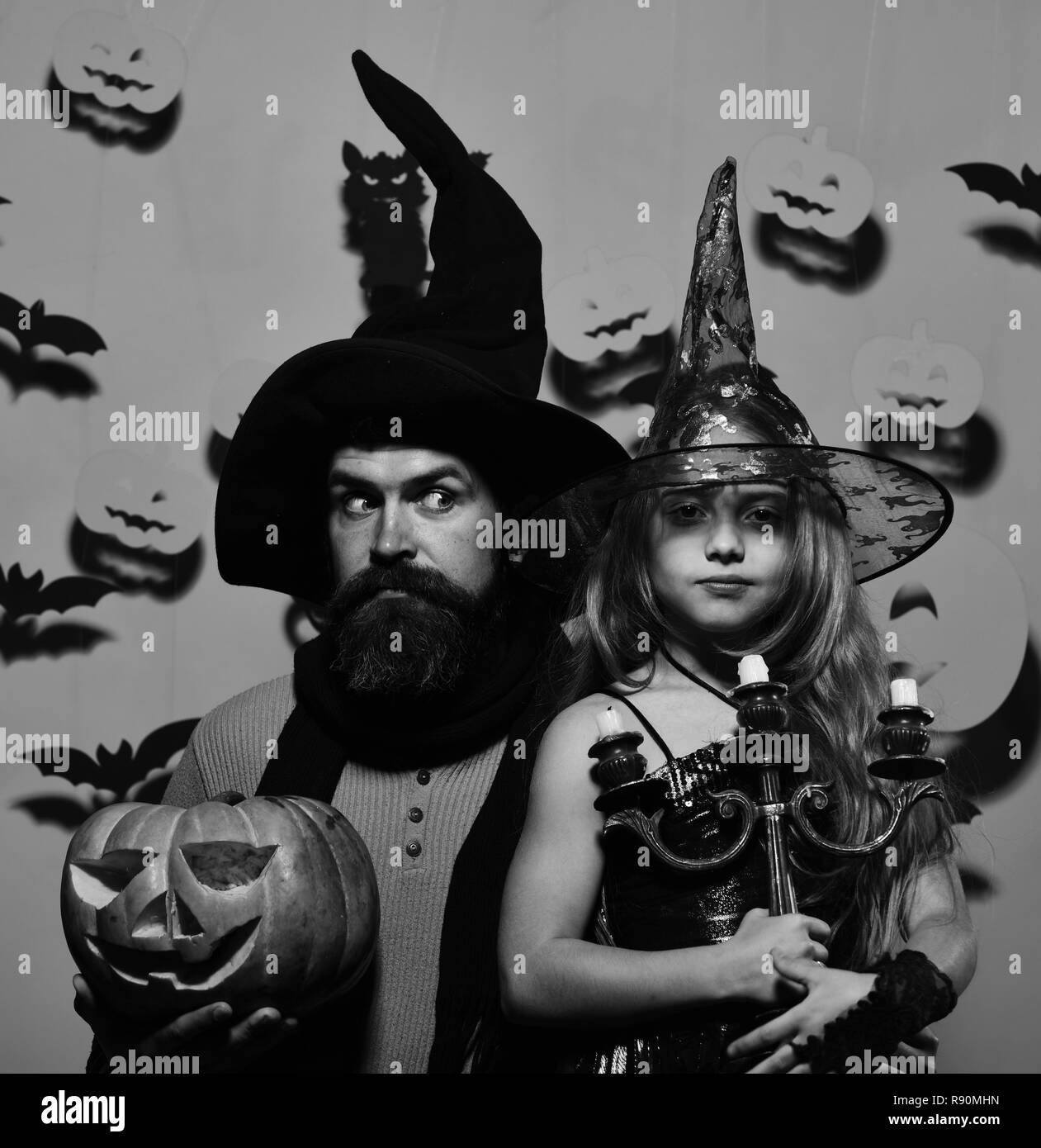 Girl and bearded man with surprised faces on pink background. Wizard and  little witch in black