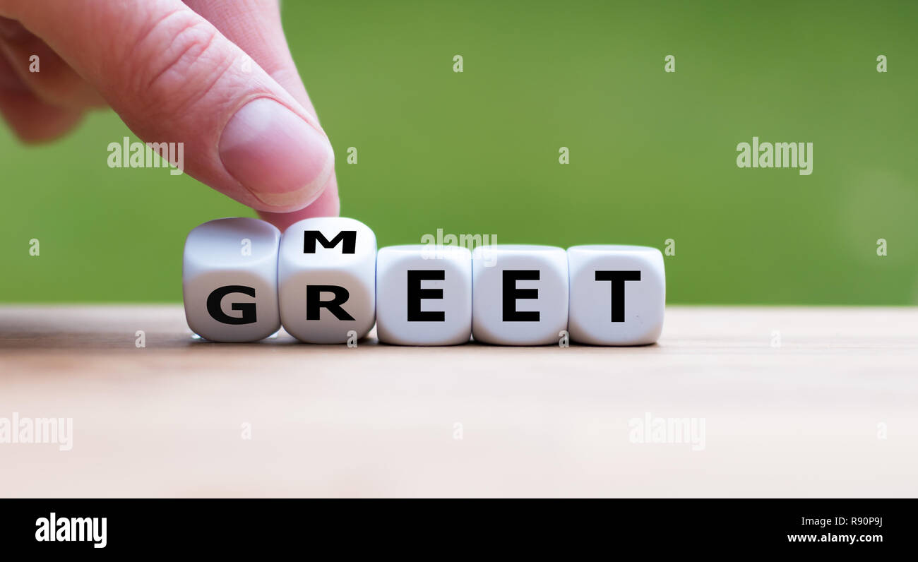 Hand is turning a dice and changes the word 'Meet' to 'Greet' Stock Photo