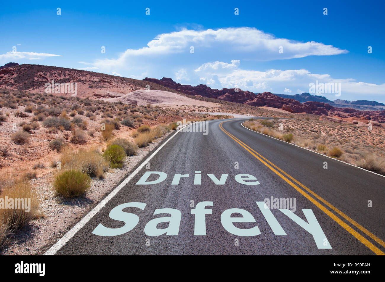 The text 'DRIVE SAFELY' written on a empty road in the desert of Nevada before the street turns right Stock Photo