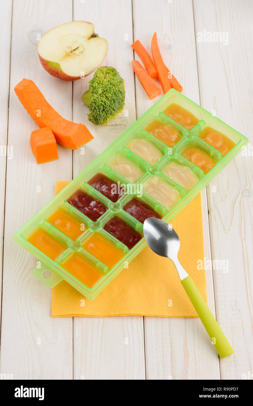 Homemade puree in freezer container, fruits and veggies on wooden table. Storage of precooked
