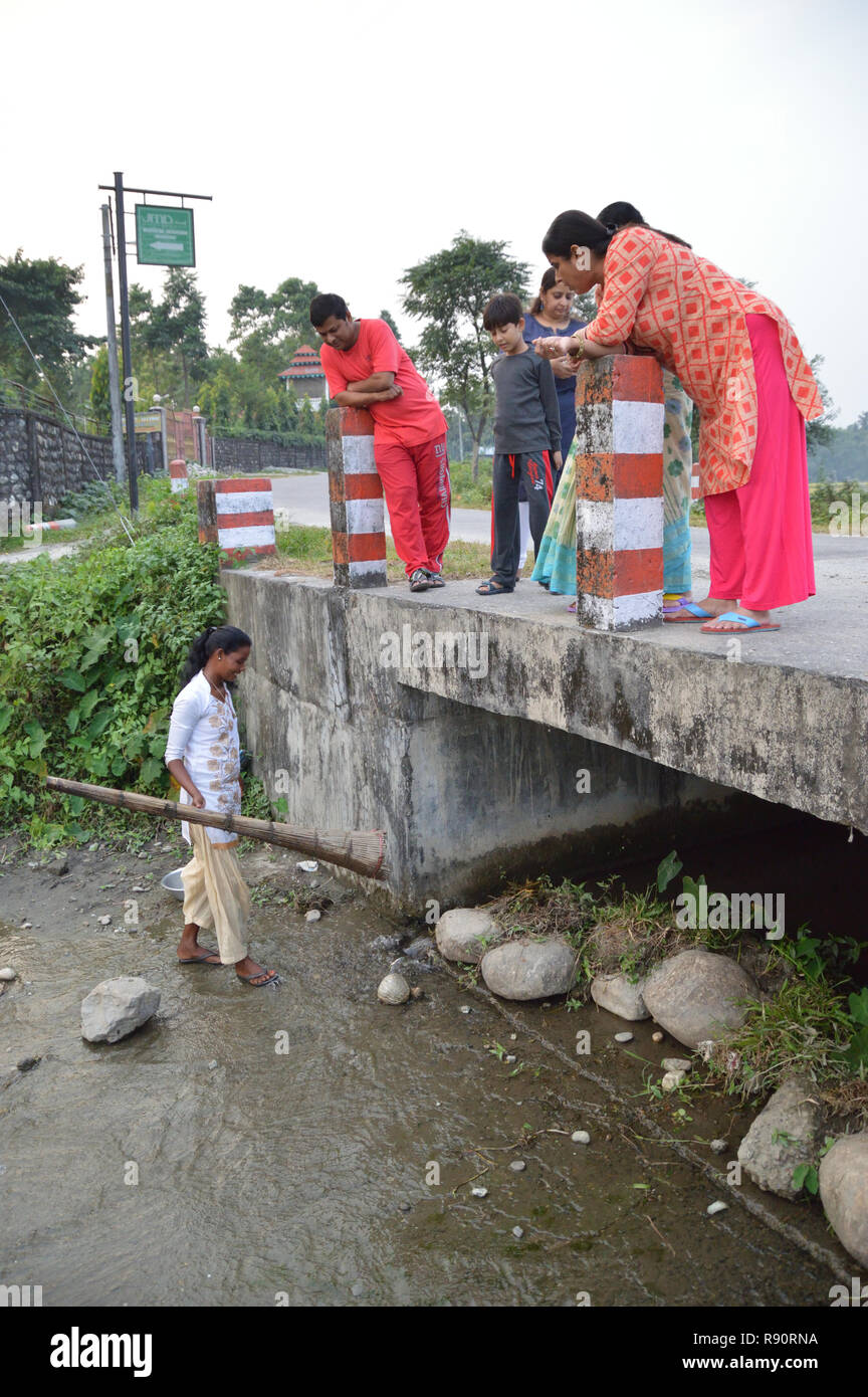 An adivasi woman sets bamboo made fish trap at the bottom of a culvert while tourists observe from road at Mangalbari bustee, Chalsa in Jalpaiguri dis Stock Photo