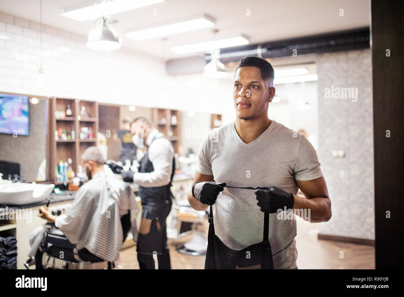 Young handsome hispanic haidresser and hairstylist standing in barber shop. Stock Photo