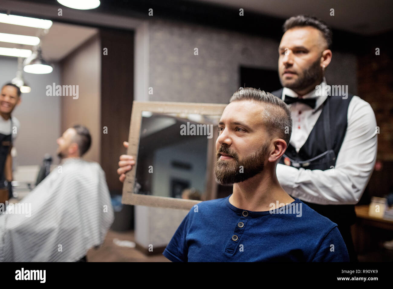 Handsome hipster man client visiting haidresser and hairstylist in barber shop. Stock Photo