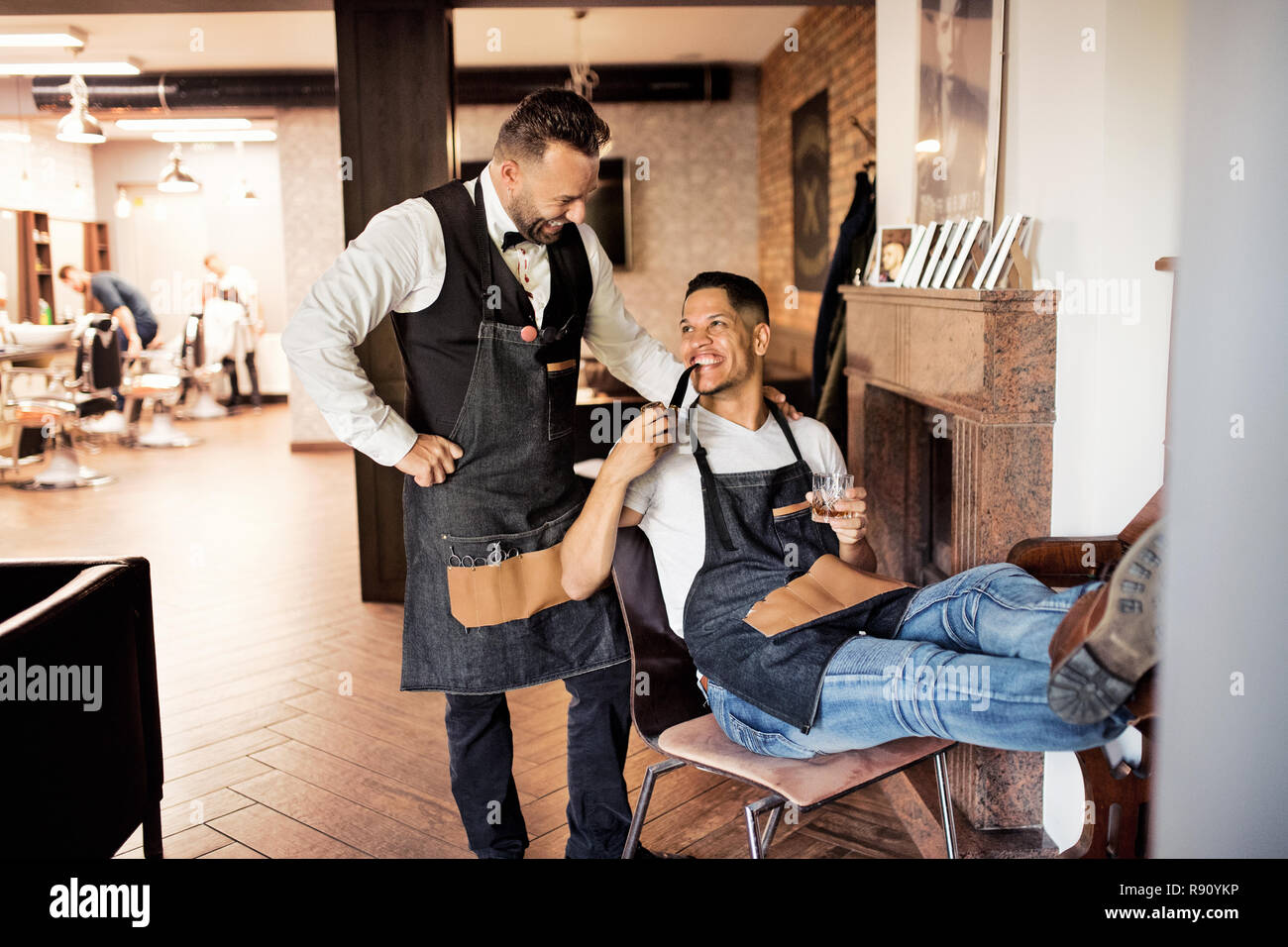 Two cheerful haidresser and hairstylist in barber shop, smoking a pipe and talking. Stock Photo