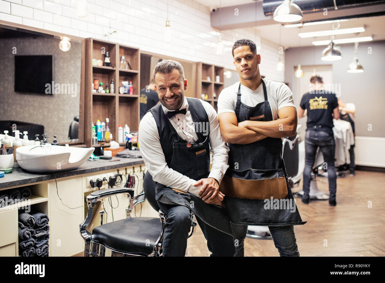 Two male haidressers and hairstylists sitting in barber shop, posing for a photograph. Stock Photo
