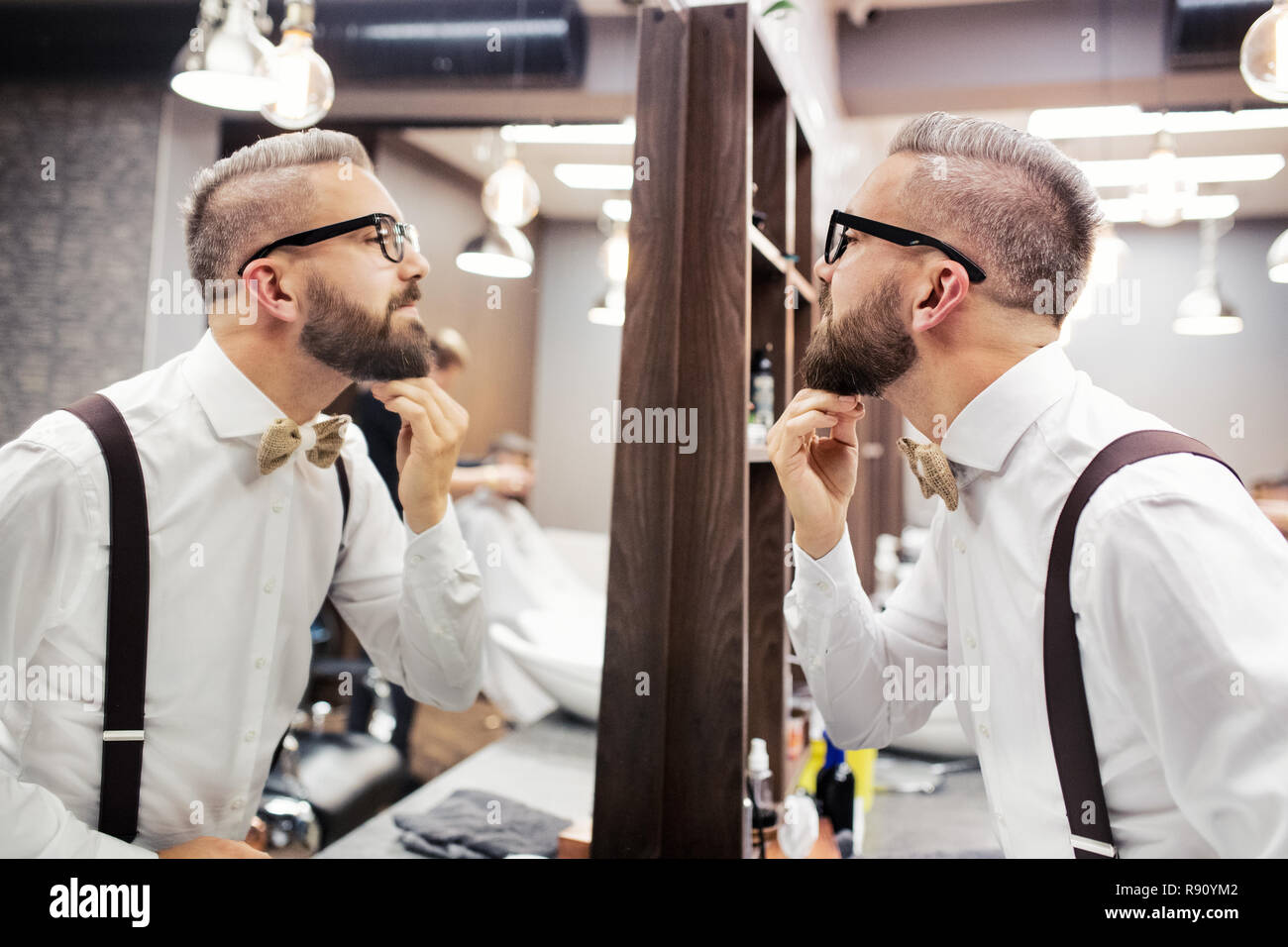 Handsome hipster man client with glasses looking in the mirror in barber shop. Stock Photo