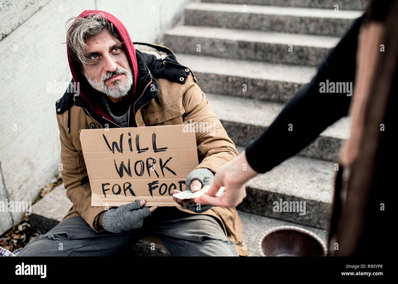 An unrecognizable woman giving money to homeless beggar man sitting in city...