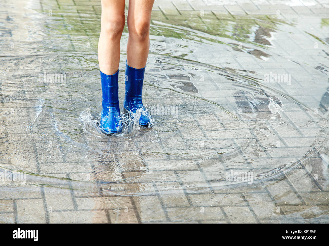 girl in blue rubber boots standing in a puddle after a rain outdoor on ...